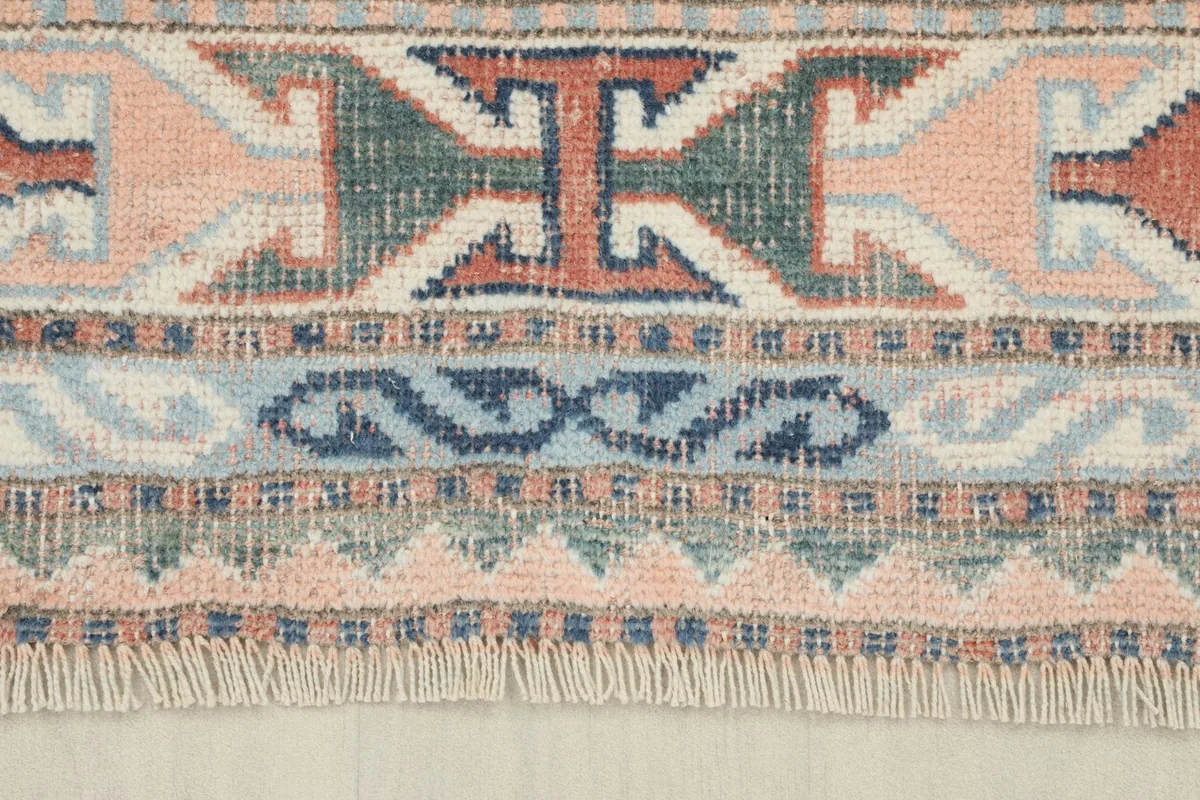 Close-up detail of the rug's border and fringe, showing the varied colors and slight wear consistent with its age.