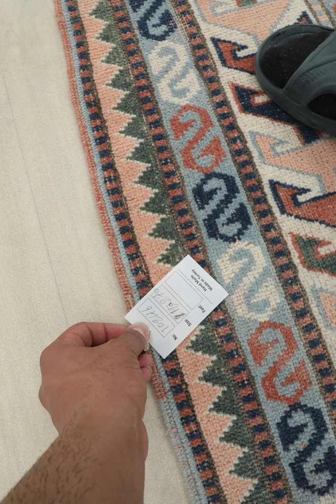A hand holding a product tag near the rug's border, indicating its quality and origin.
