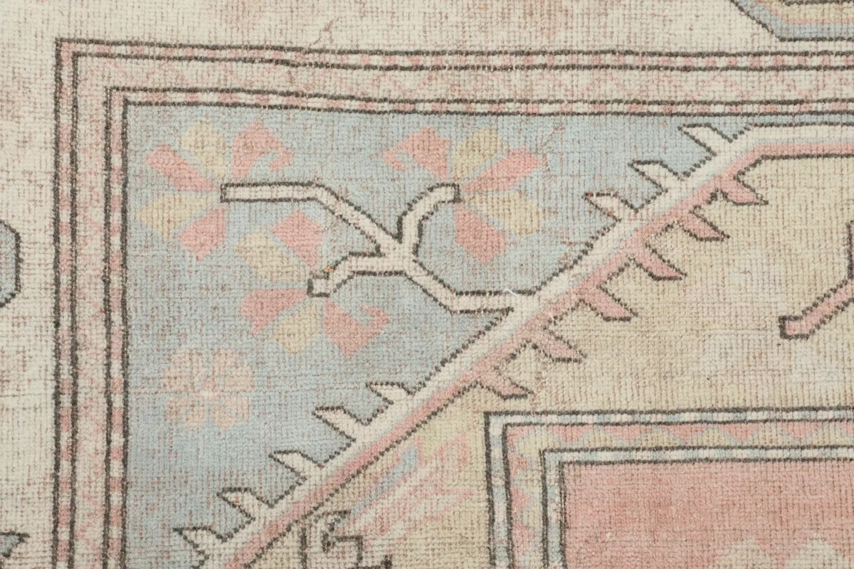Detailed shot of the rug's border, displaying the geometric patterns in blue, beige, and rose