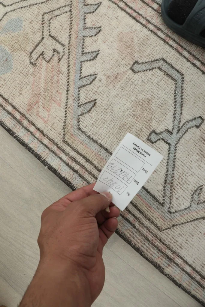 Hand holding a tag on the rug, indicating its size and origin details