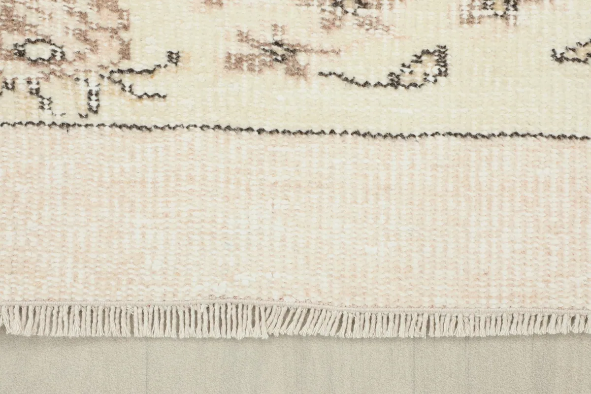 View of the rug's short, natural ivory fringe and the edge of the cotton foundation