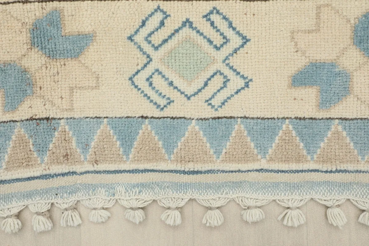 Detail of the rug's border with blue, beige, and ivory geometric shapes and fringe
