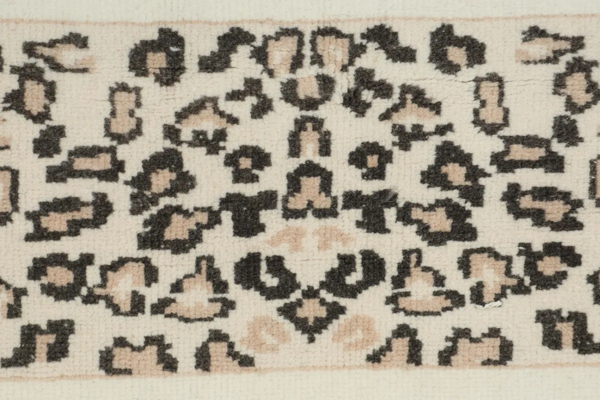 Close-up detail of the hand-knotted leopard pattern in black and beige on the ivory pile.