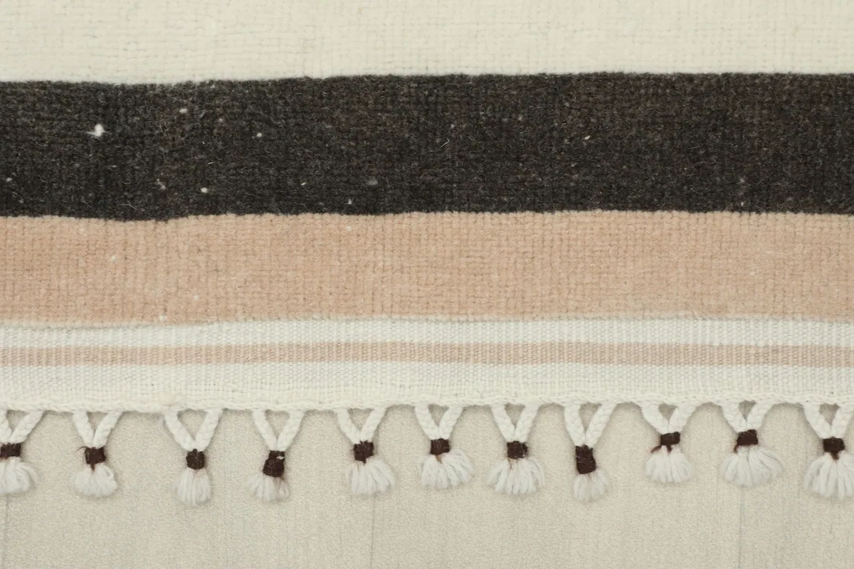 Detailed view of the outer black and beige striped border and fringe.