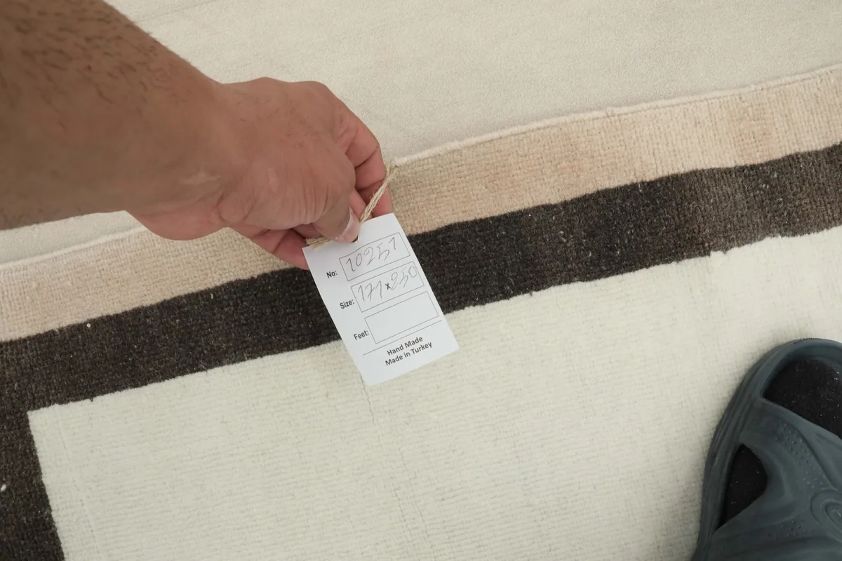 Hand holding a product tag, showing the rug's details and 'Hand Made in Turkey' label.
