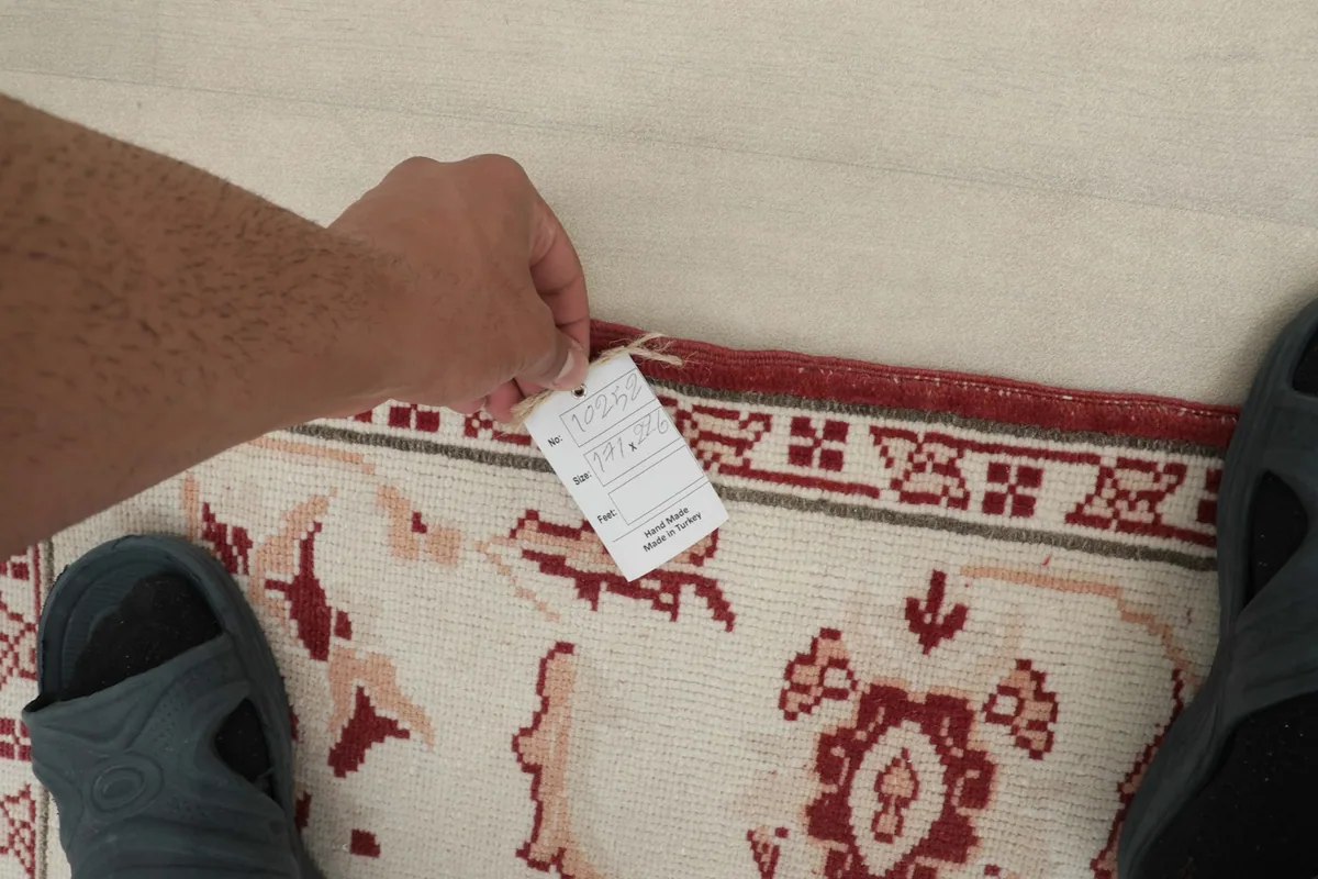 Hand holding a tag near the rug's border, showing the quality and origin.