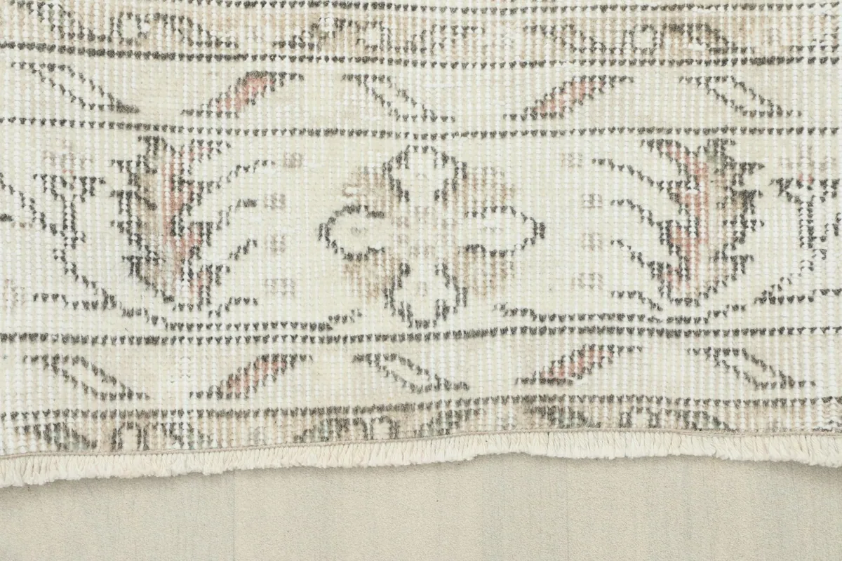 Detailed view of the rug's border, featuring intricate gray patterns on a cream background.