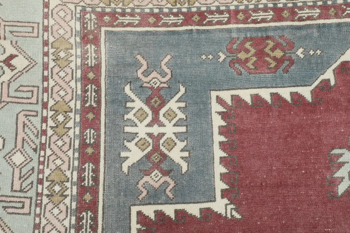 Detailed view of the rug's border, featuring intricate geometric designs in red, beige, and olive tones.