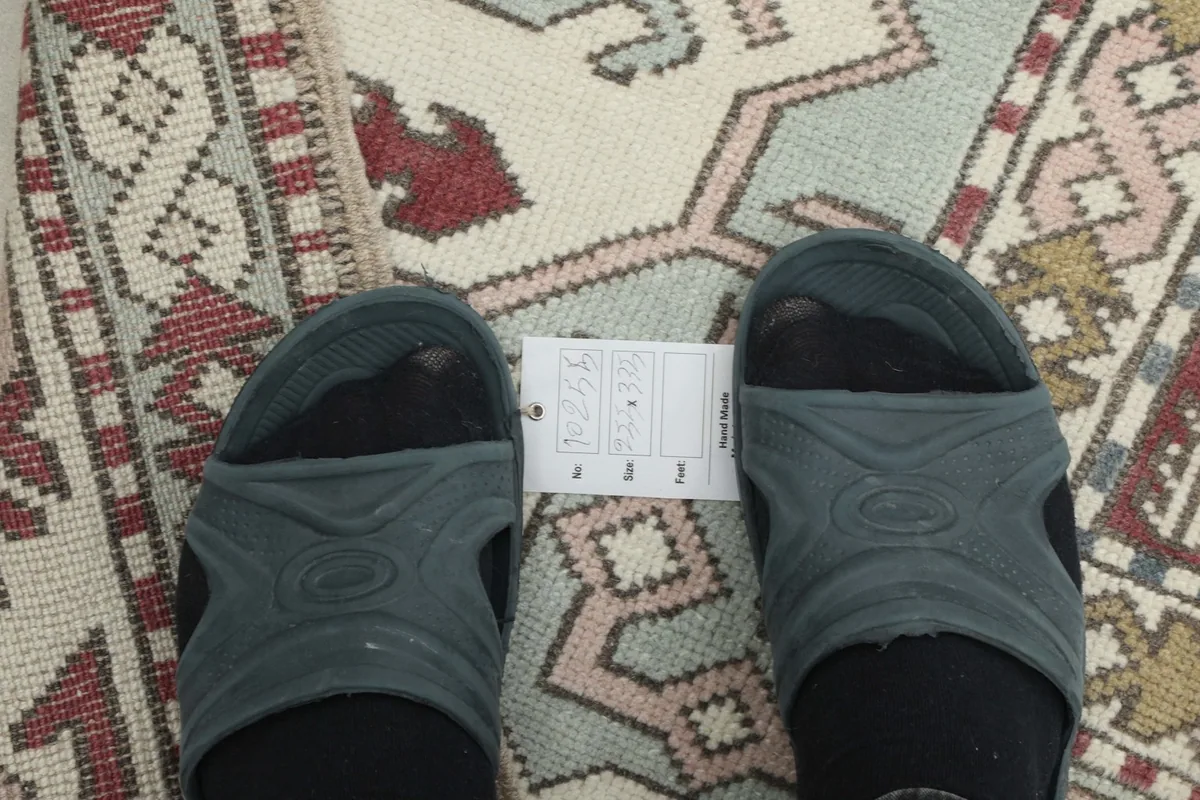 Close-up of the rug's low wool pile texture with a shoe for scale, showing the intricate weaving.