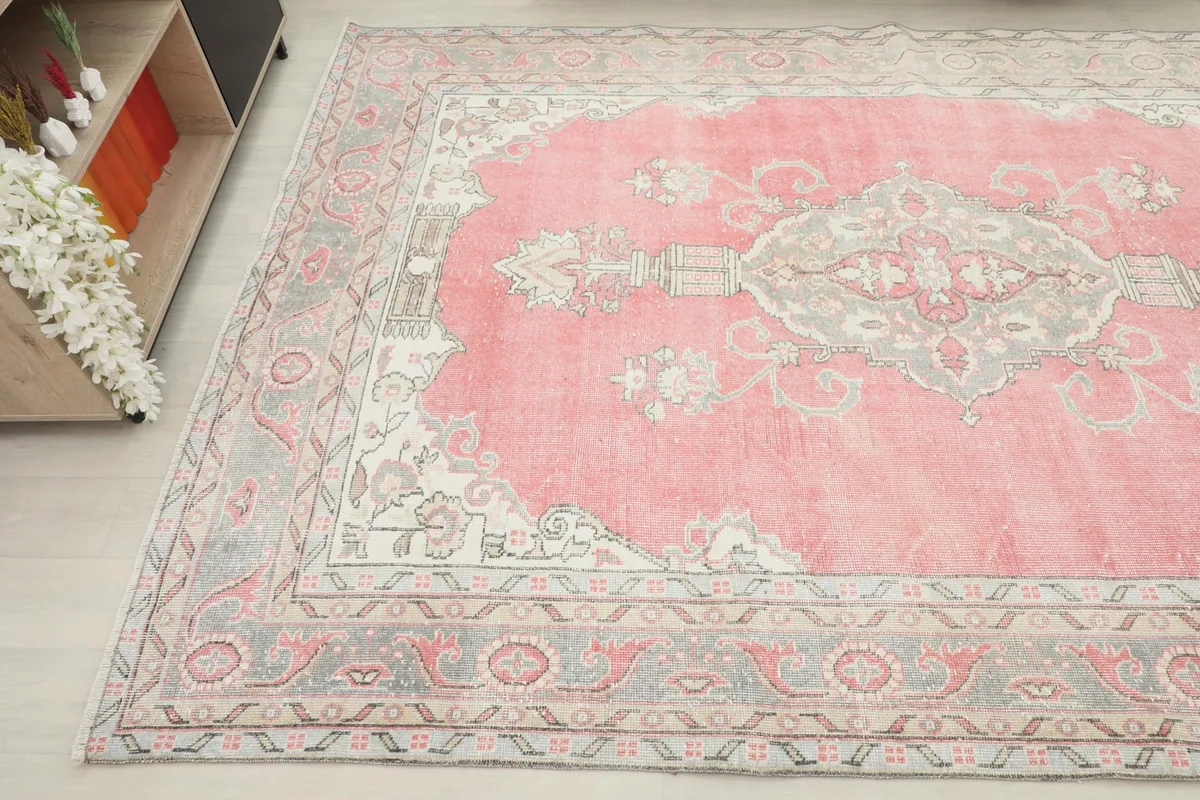 Angled view showing a section of the pink rug with its detailed border and a cabinet in the background