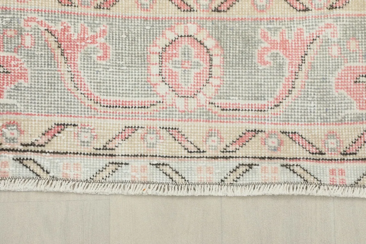 Detailed view of the rug's border pattern, revealing the intricate gray, pink, and beige designs
