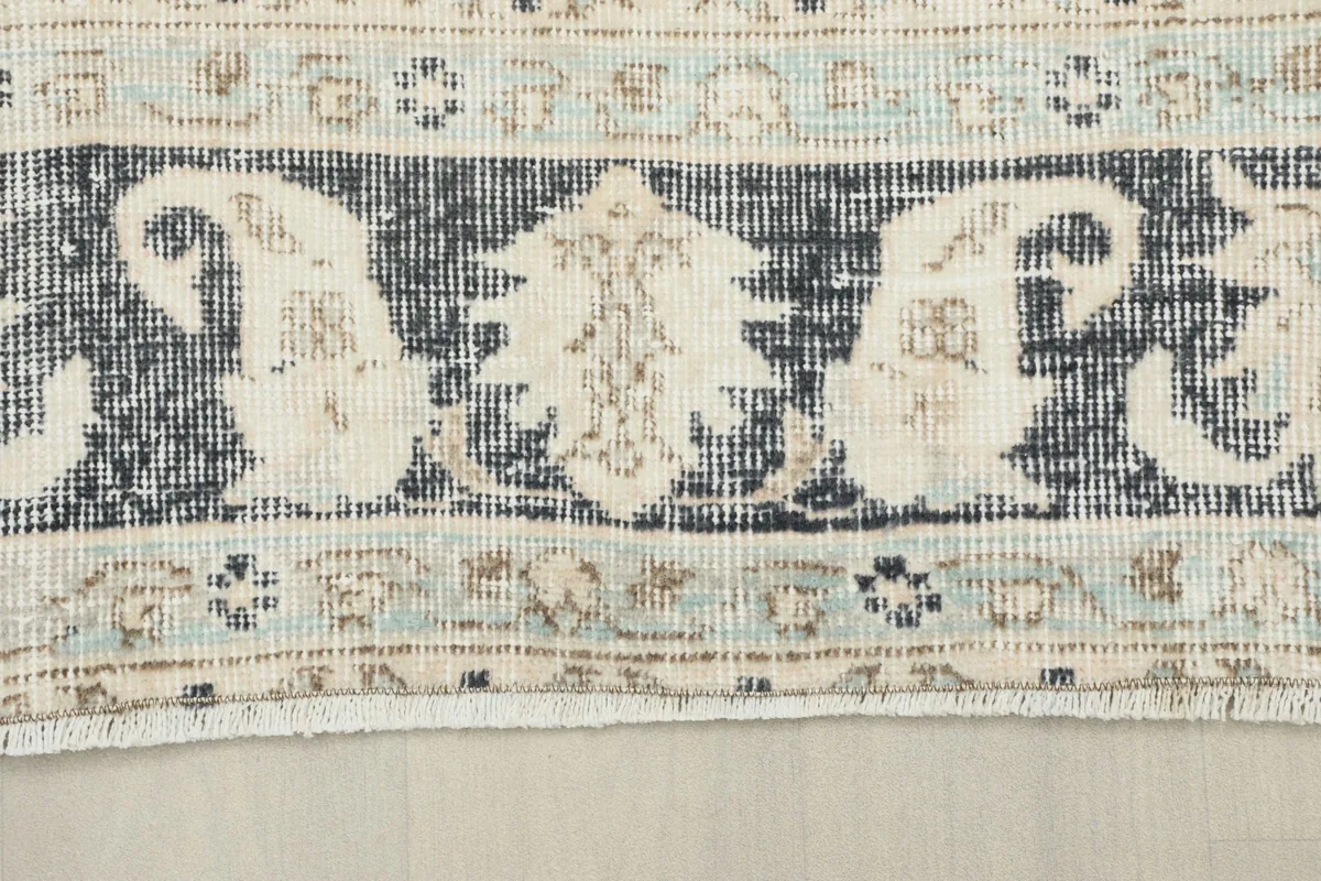 Close-up of the charcoal border with ivory paisley-like patterns and a thin inner beige stripe.
