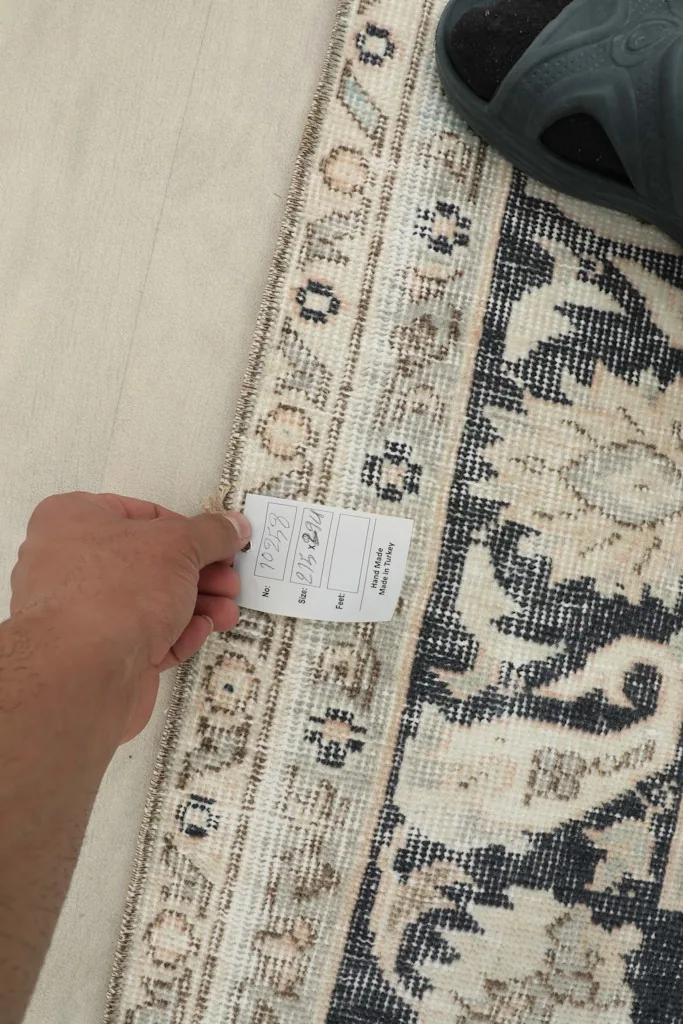 Hand holding a tag near the rug's border, showing the texture and pattern close up.