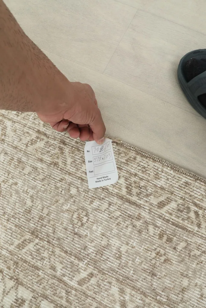 A hand holding a tag, showing the rug's edge and the hand-knotted detail.