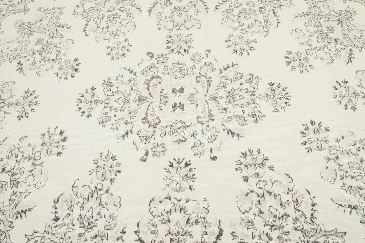 Close-up of the central botanical motif on the ivory vintage rug, showing the softened gray and brown colors.