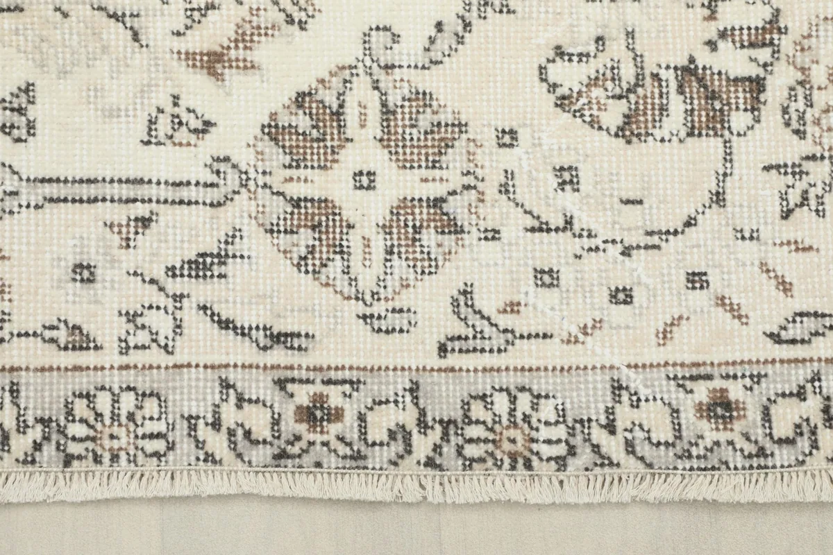 Close-up of the rug's border and a section of fringe, revealing the gray and ivory tones and weave.