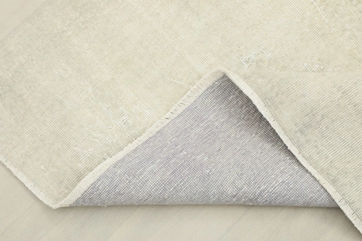 Corner of the rug folded back, revealing the cotton foundation on the reverse side.