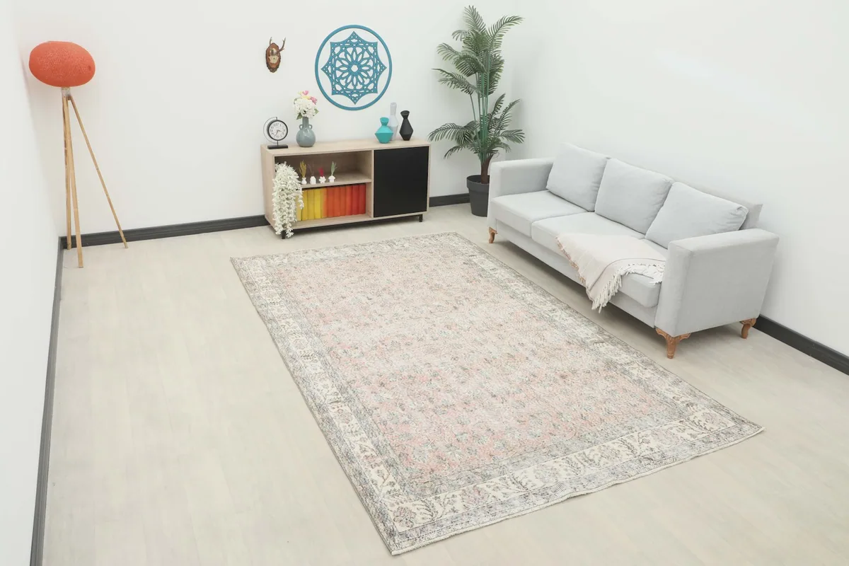 Wide shot of the large rose and ivory rug placed in a modern living room setting with a gray sofa.