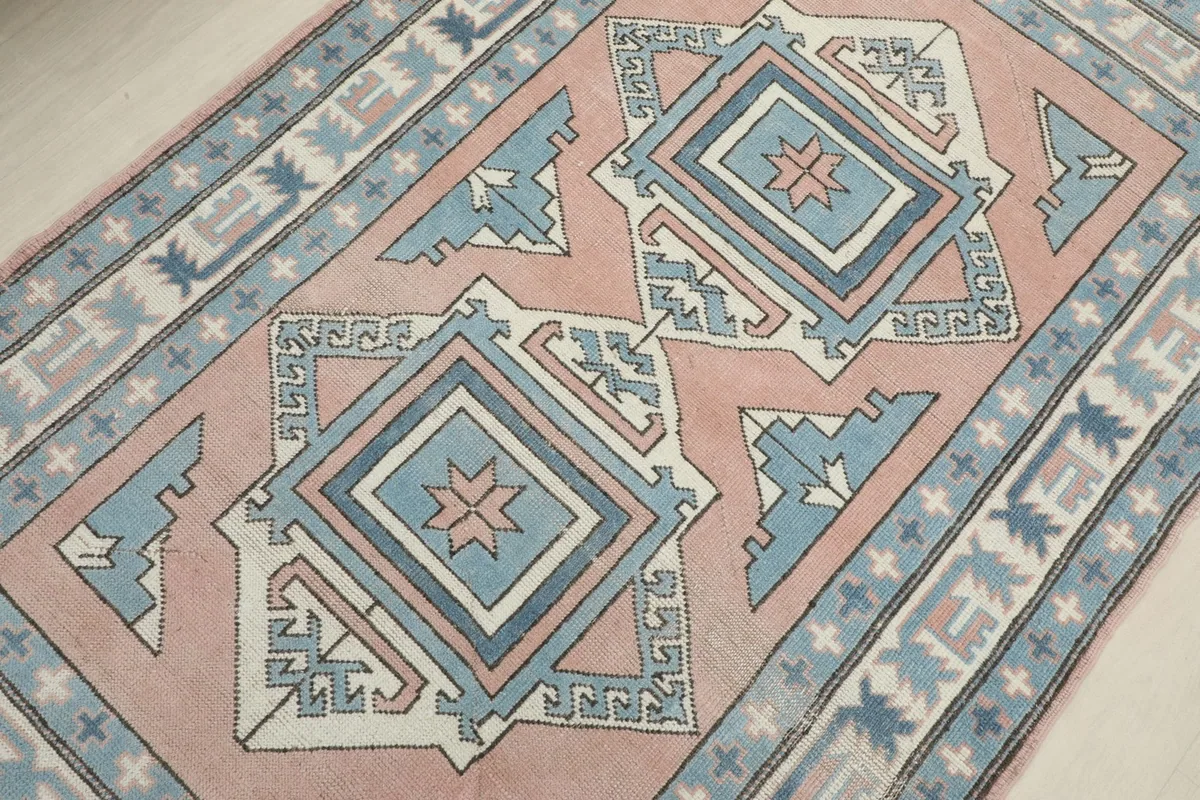 Detailed angle shot of the rug's central geometric motifs in rose, blue, and ivory tones.