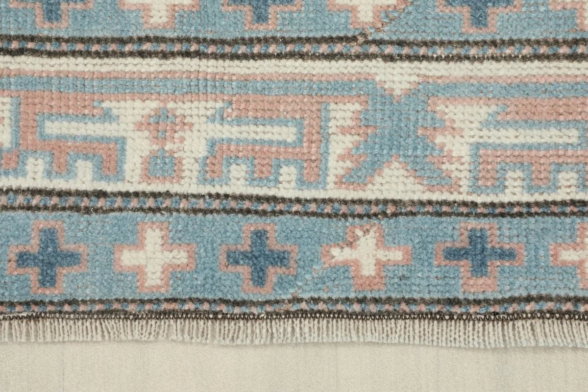 Detailed view of the intricate blue and ivory border patterns and fringe of the rug.