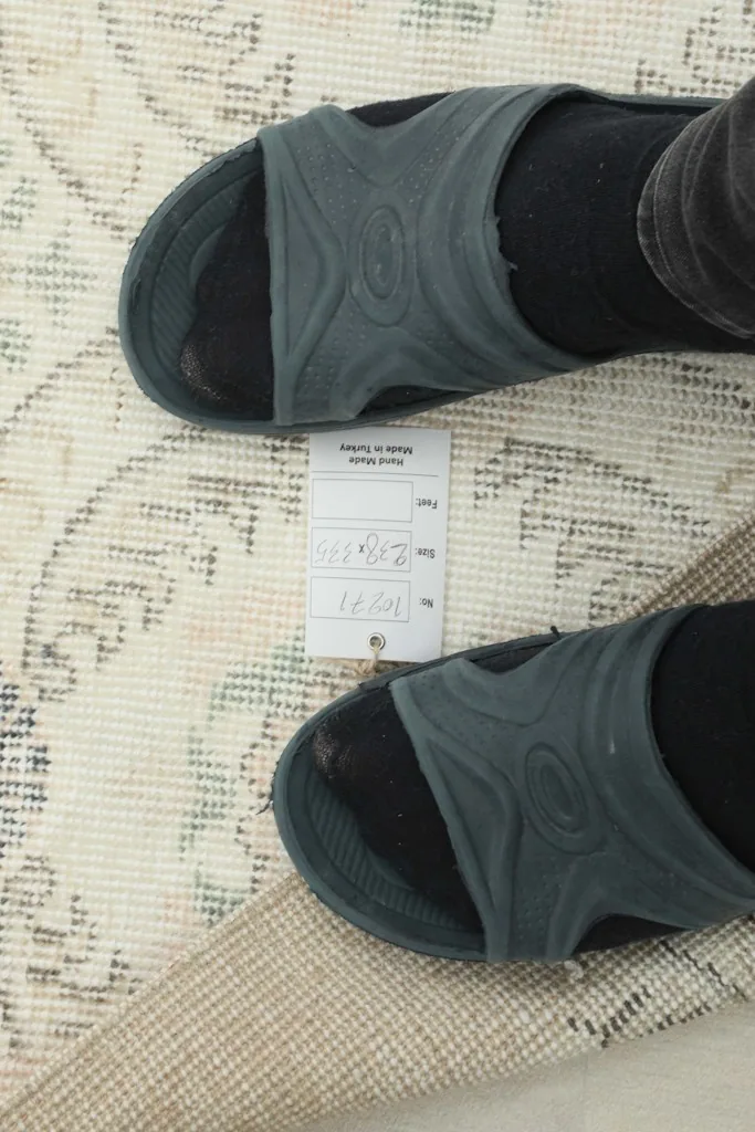 Overhead view of the rug with a tag, showing the soft texture and scale next to feet.