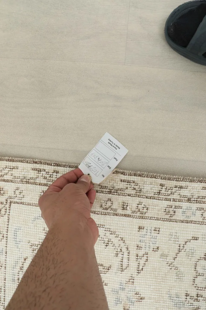 Hand holding a product tag near the rug's border, showing the texture and fringe