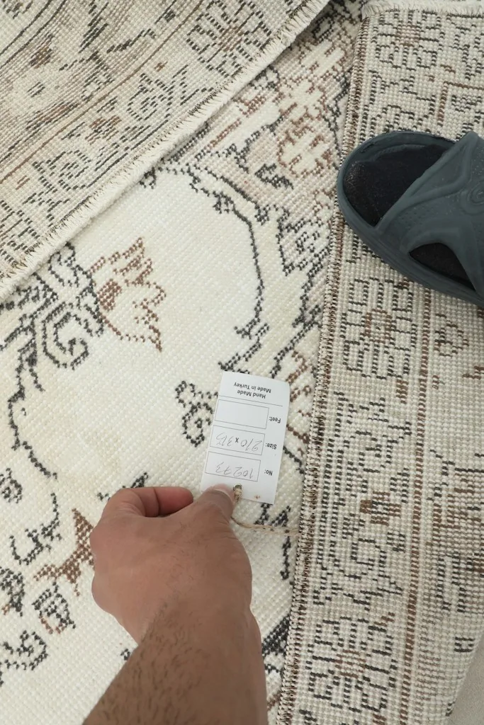 Hand holding a tag near the back of the rug, showing the knotting and foundation