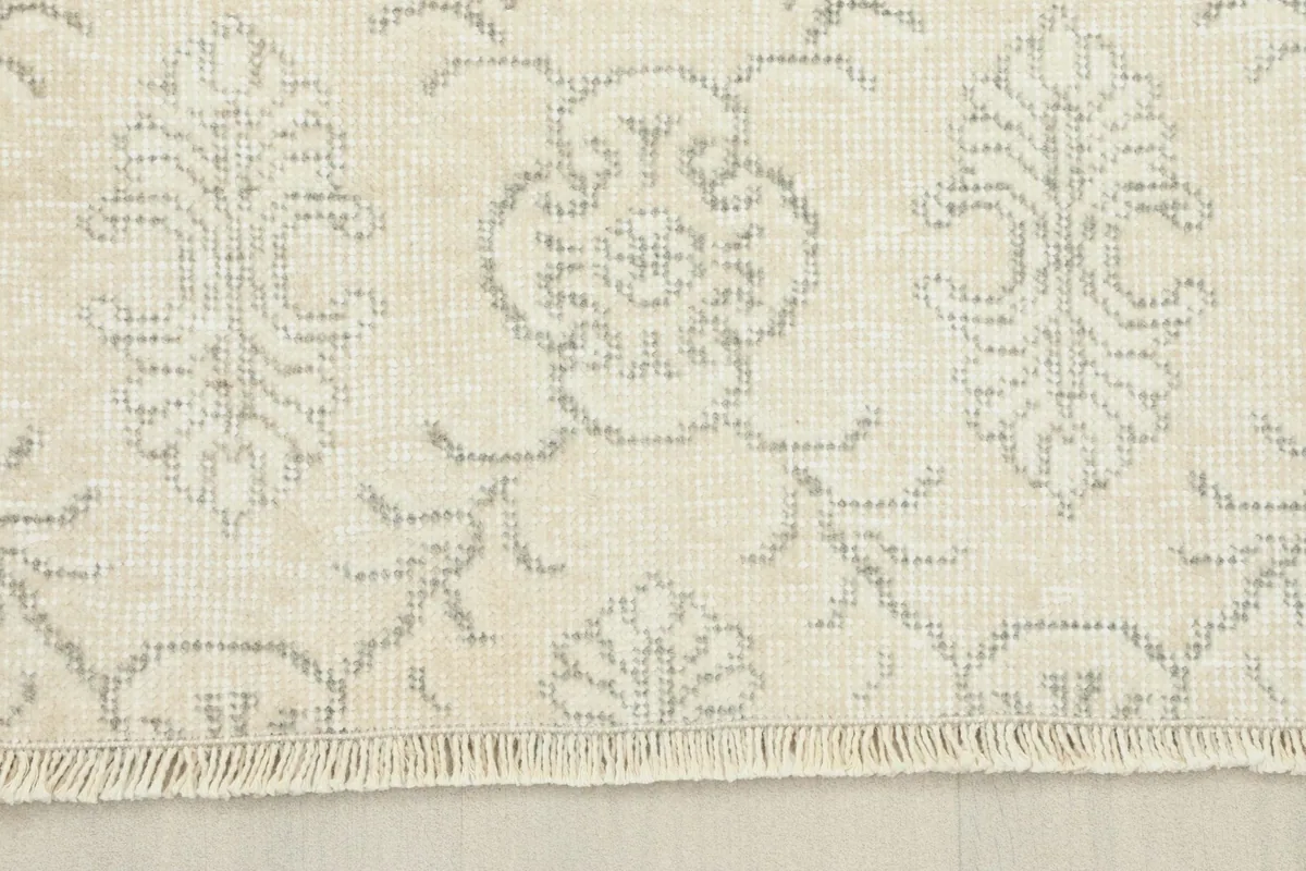 Detail view showing the short, natural fringe and the knotting along the edge of the ivory rug.