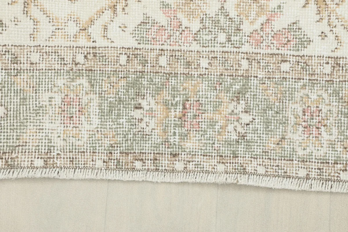 Detail of the rug's border, showing the olive and gray tones with small floral elements