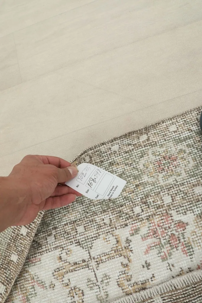 Hand holding a tag near the rug's edge, showing the texture of the pile