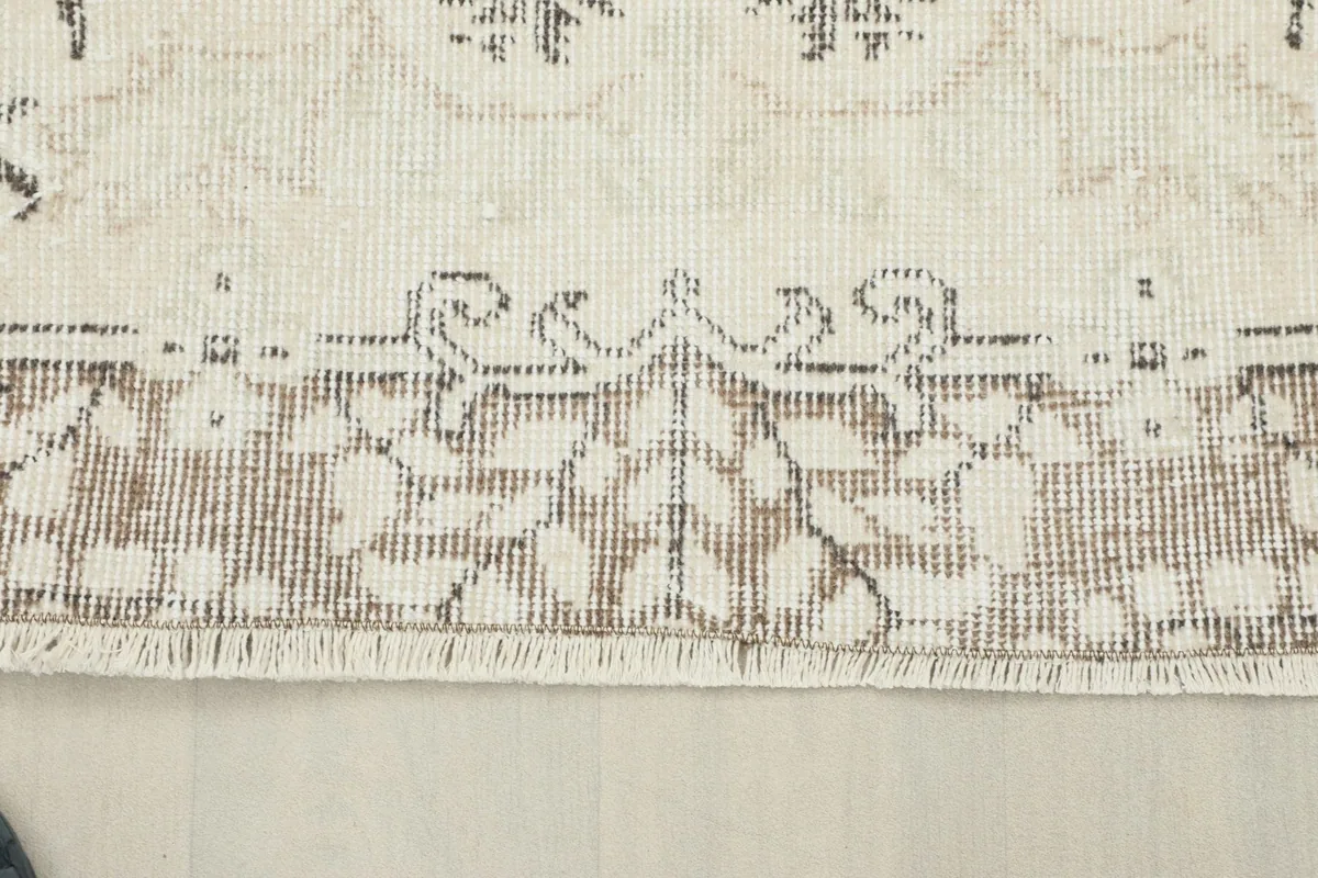 Close-up of the beige and cream border design and short fringe of the hand-knotted wool rug