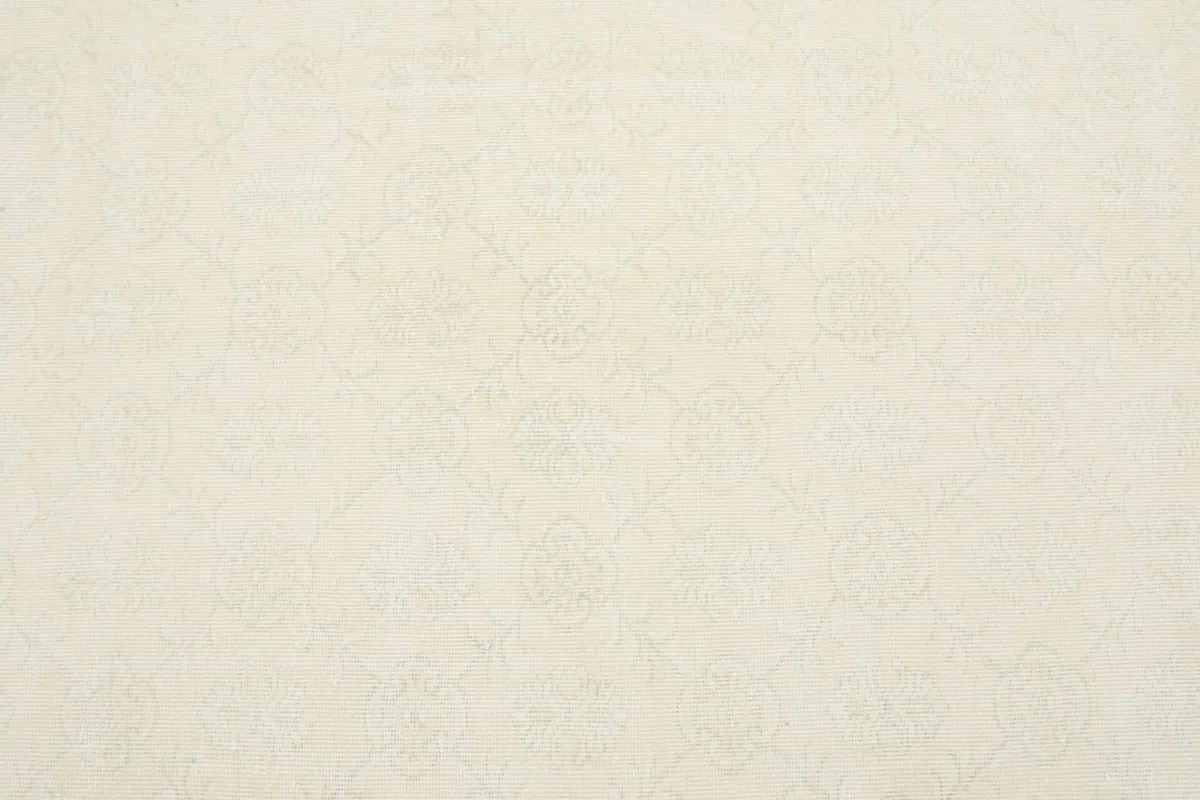 Detailed overhead view revealing the very subtle, faded floral and geometric patterns on the ivory rug.