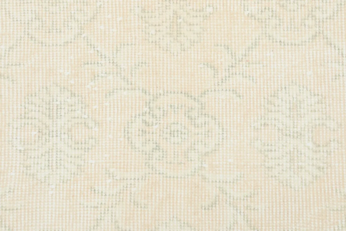 Close-up detail of the faded floral motifs and low pile texture on the vintage ivory wool rug.