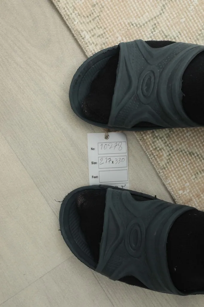 Overhead view with a size tag and sandals for scale, showing the rug's texture and color.