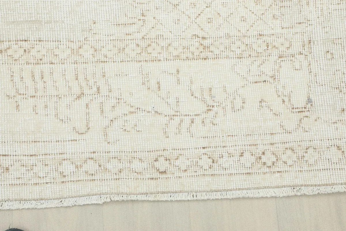 Detail of the rug's border, revealing intricate geometric patterns in muted tan and beige tones