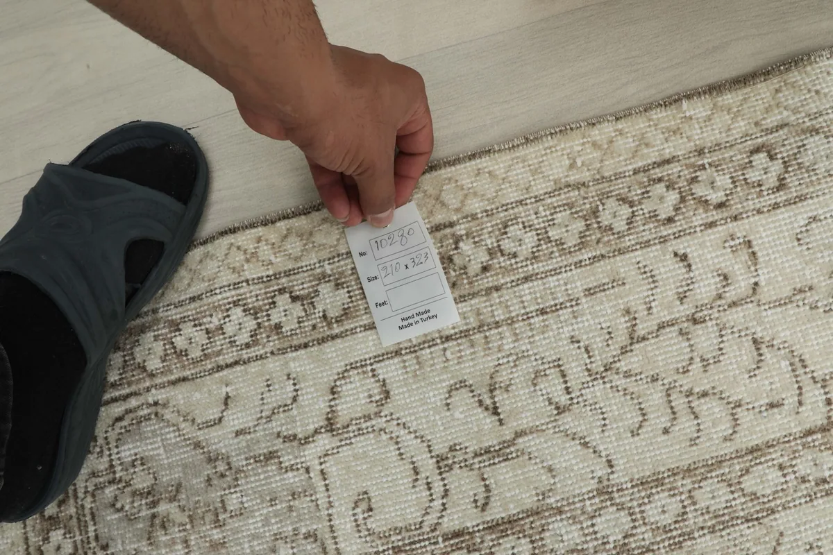 Hand holding a tag on the rug, showing a close-up of the border patterns and texture