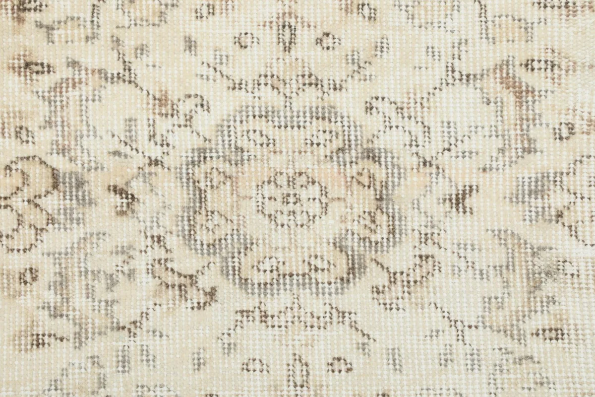 Detailed view of a central medallion motif and surrounding floral elements in gray on an ivory background.