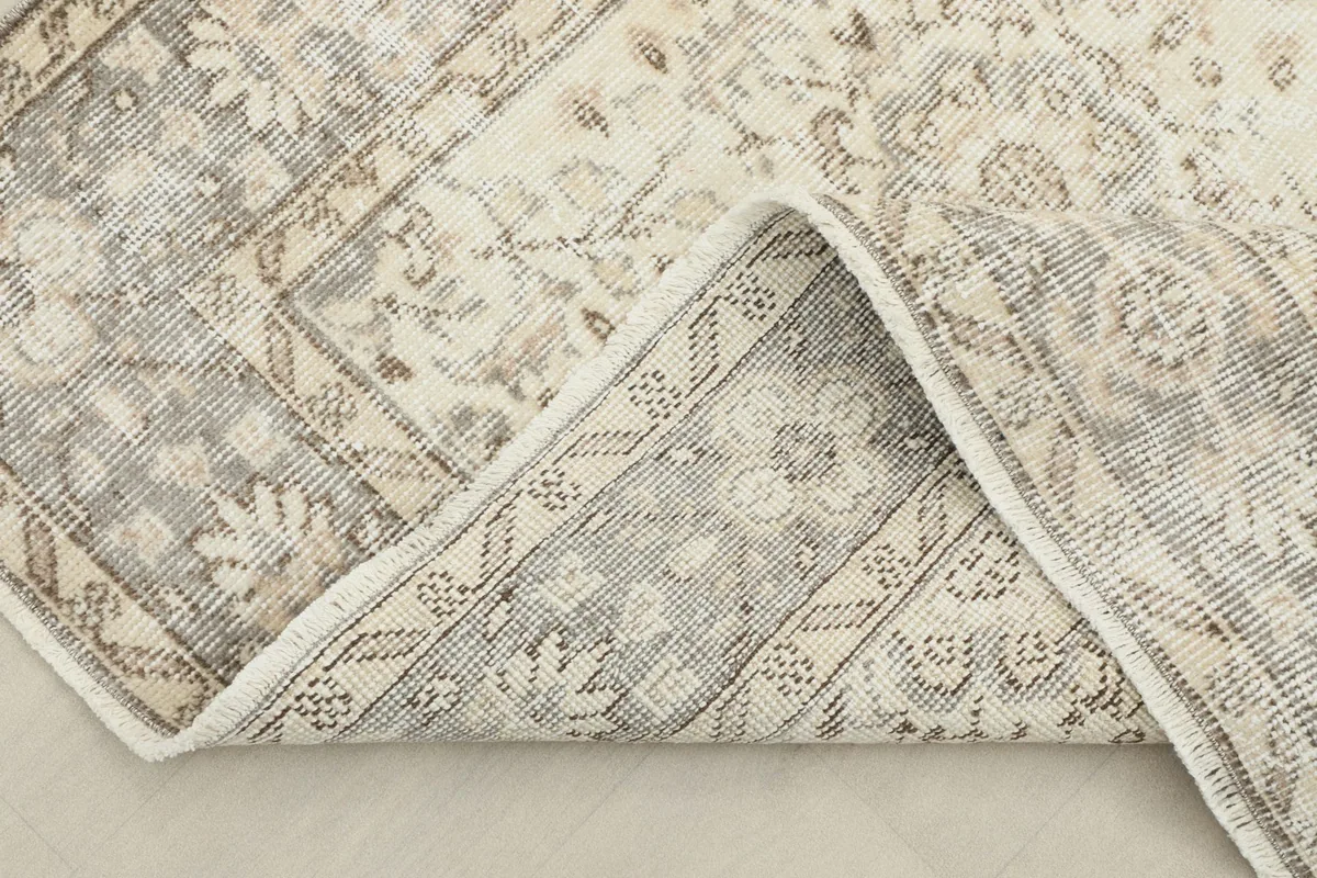Corner of the rug folded back, showing the back of the hand-knotted cotton foundation.