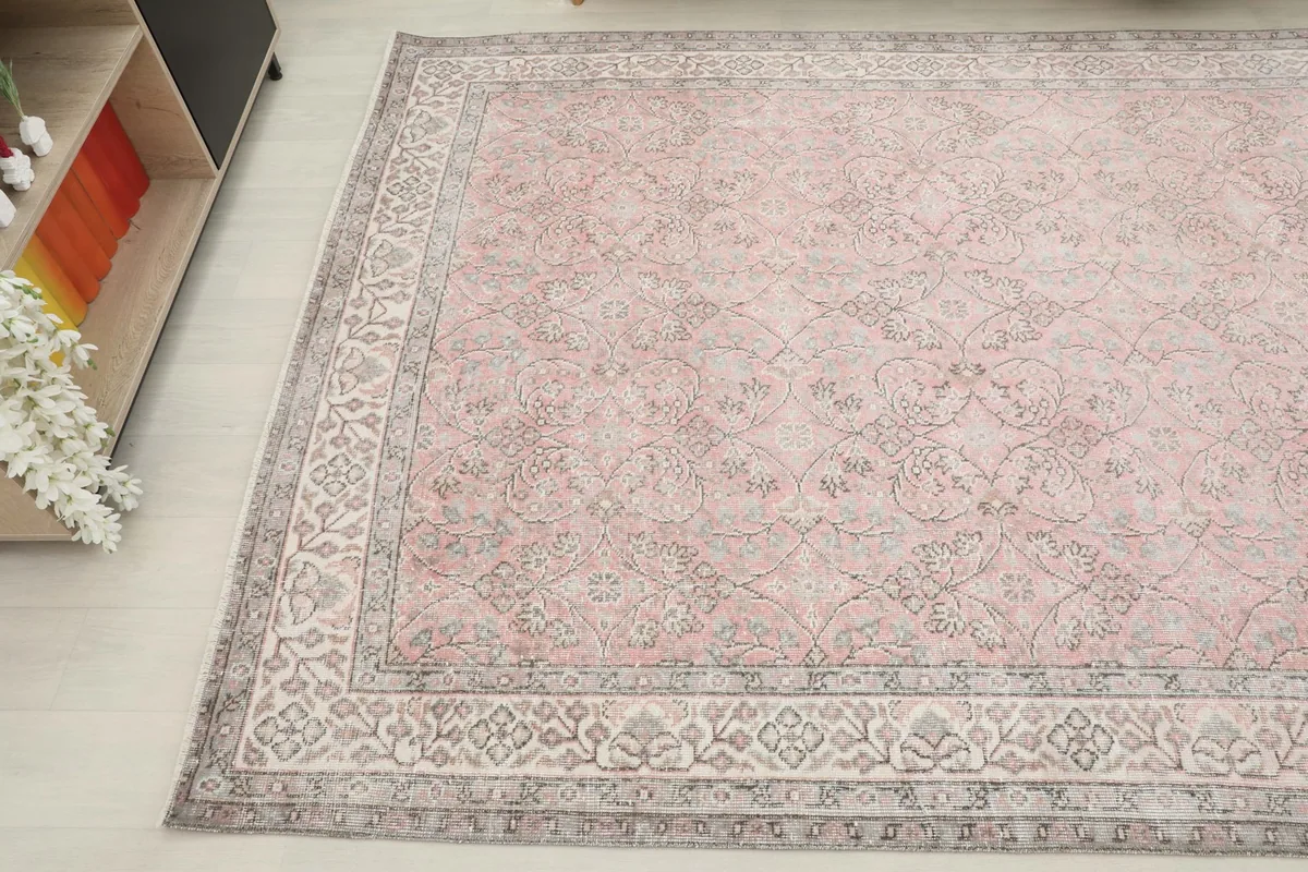 Angled shot of the vintage rug, showcasing its soft rose color and decorative gray border.