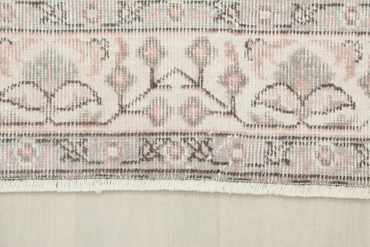 Close-up of the intricate gray and beige border design and the short fringe of the vintage rug.