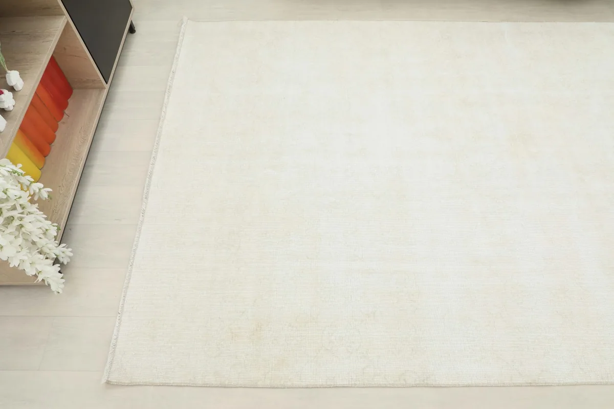 Overhead angled shot of the ivory rug in a room, showing its placement next to a furniture piece.