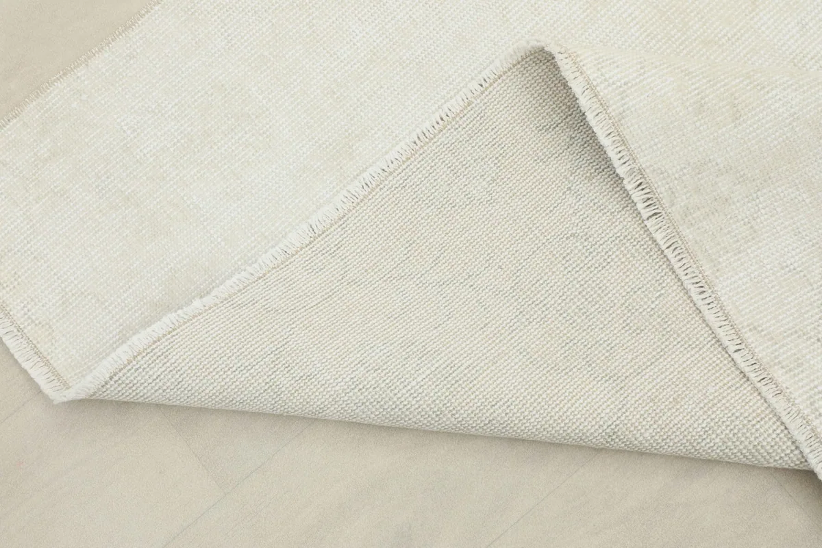 Corner of the ivory rug folded back to display both the wool pile and the cotton foundation.