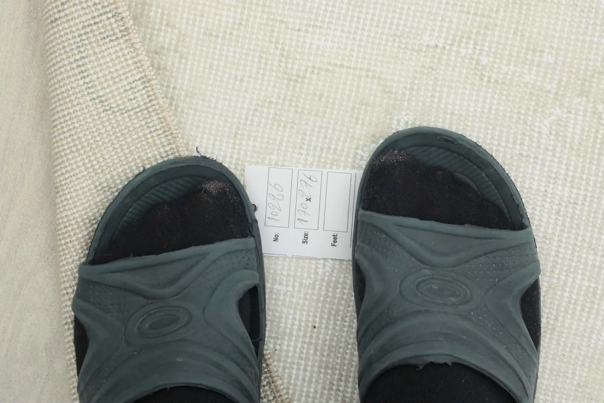 Feet in sandals next to a size label placed on the rug, indicating the rug's dimensions and scale.