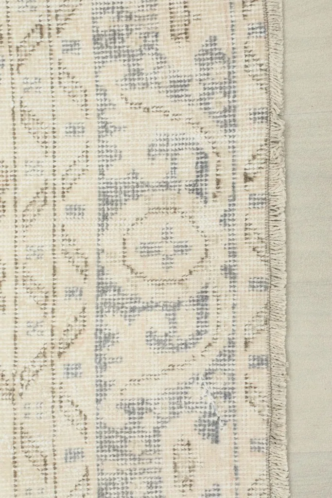 Edge detail of the rug showing the gray patterned border and the short, natural fringe