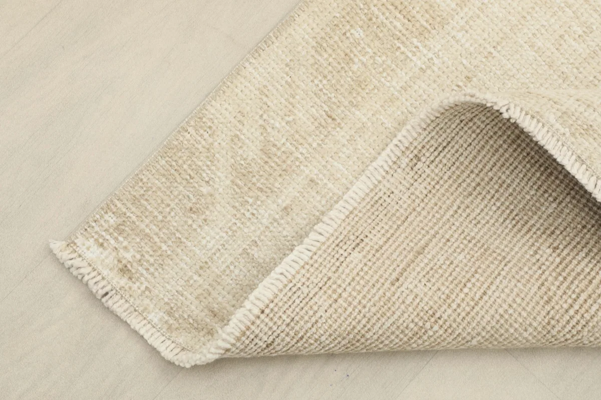 Corner of the rug folded back to show the reverse side, displaying the hand-knotted cotton foundation.