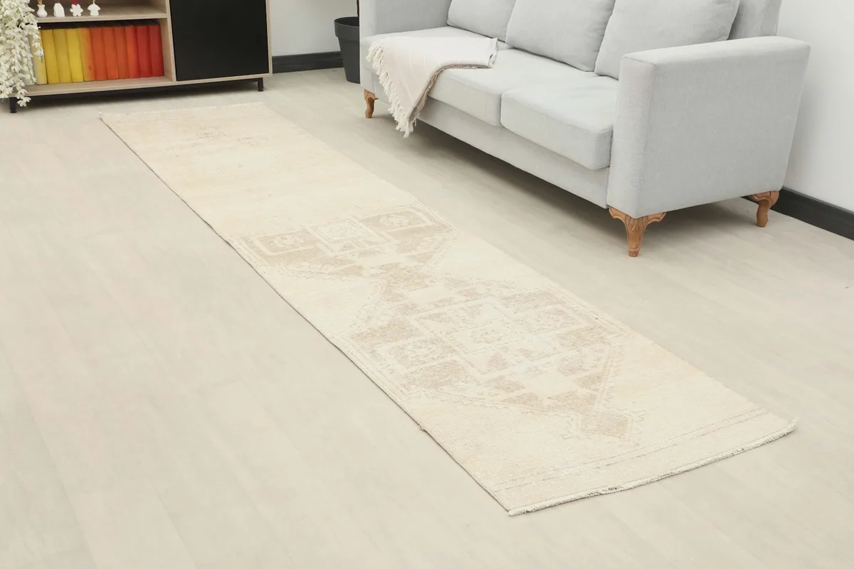 Angle view of the ivory and beige runner rug in a room, showing its length and placement next to a light gray sofa.