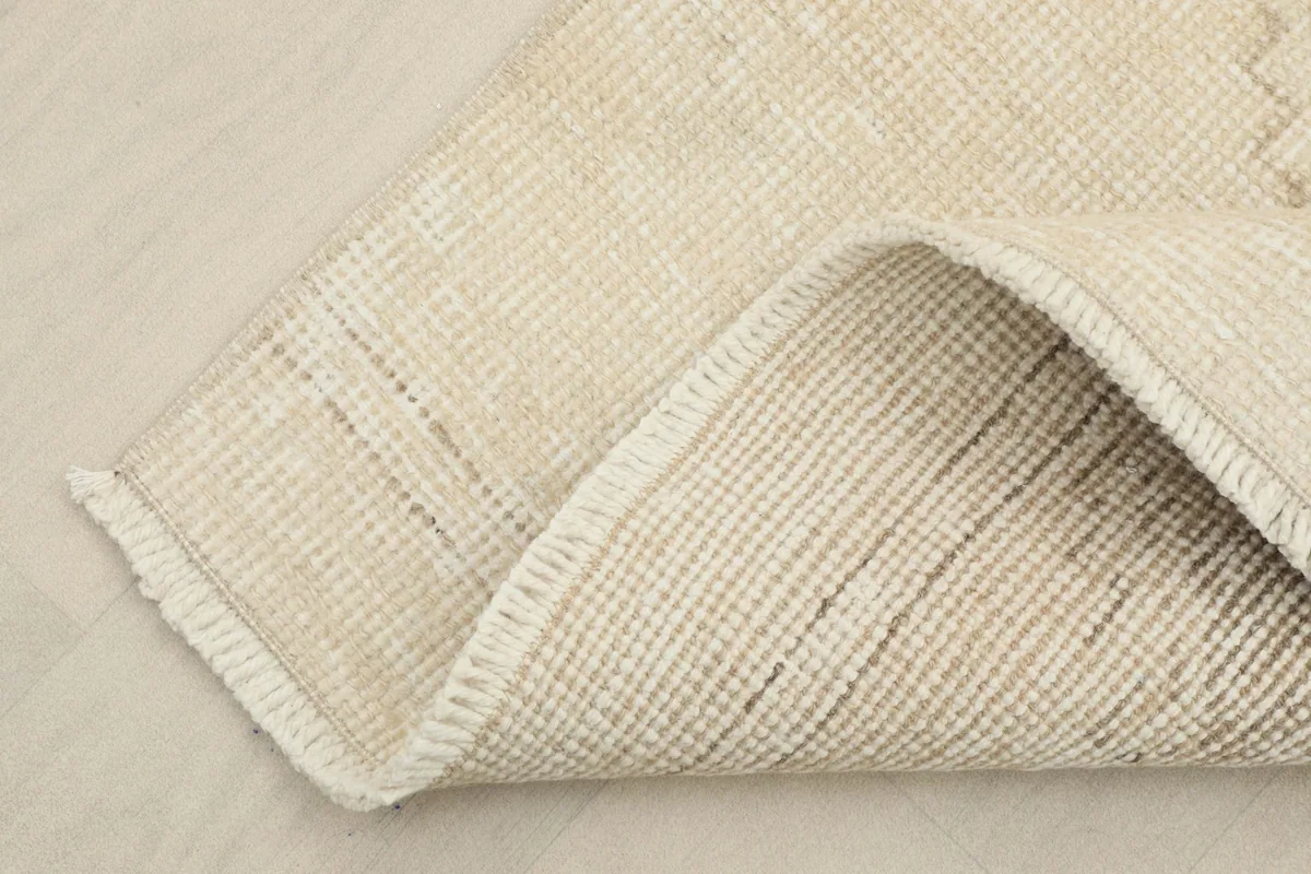 A corner of the runner rug folded back to reveal the cotton foundation and the reverse side of the hand-knotting.