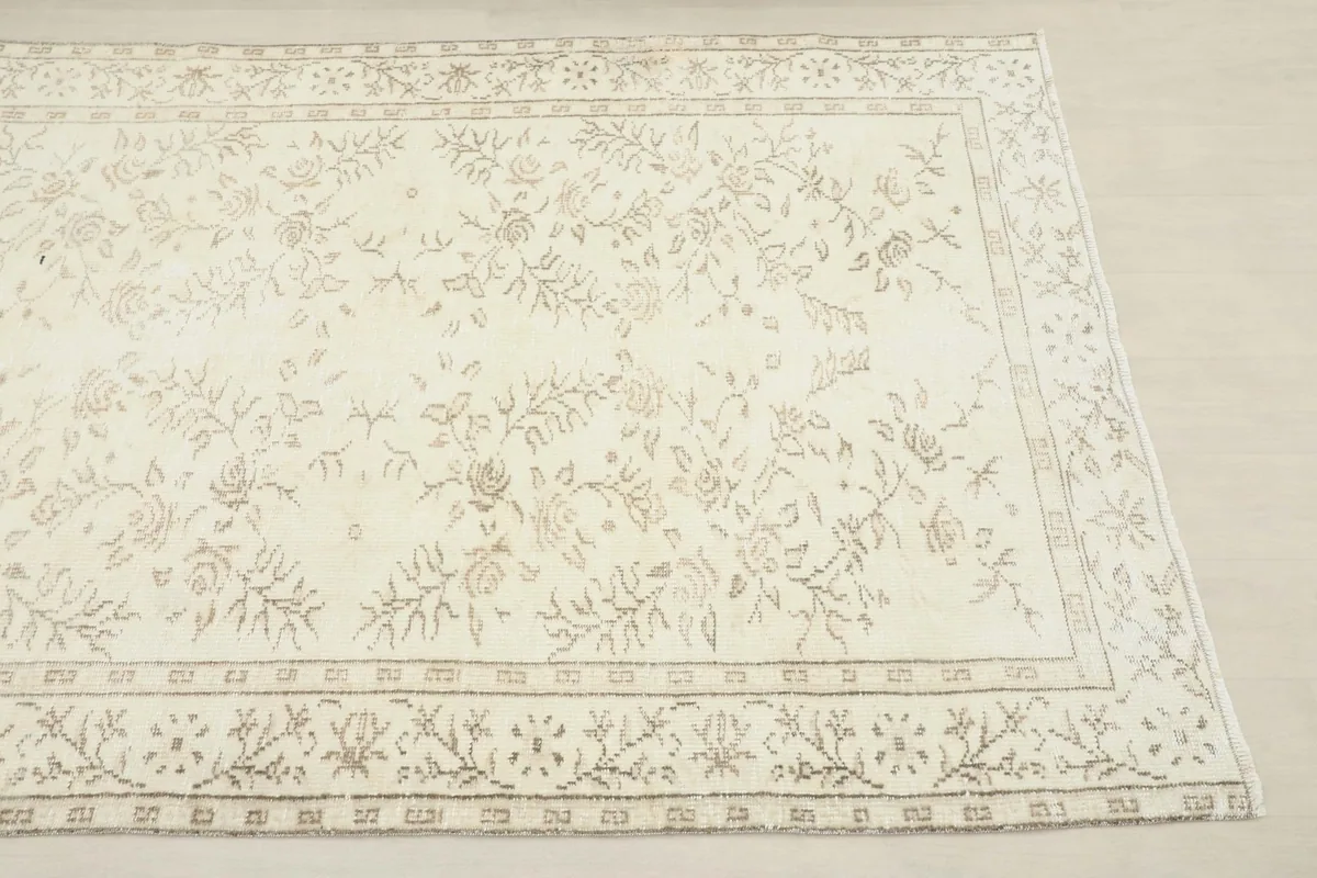 Close-up angled view of the rug's corner, showing the ivory field and tan floral motifs.