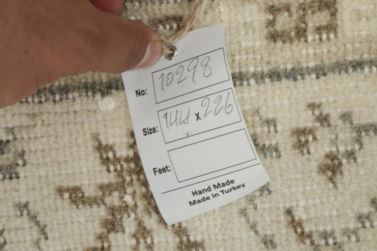 Hand holding a tag showing rug details like size (144x226 cm) and 'Hand Made in Turkey'.