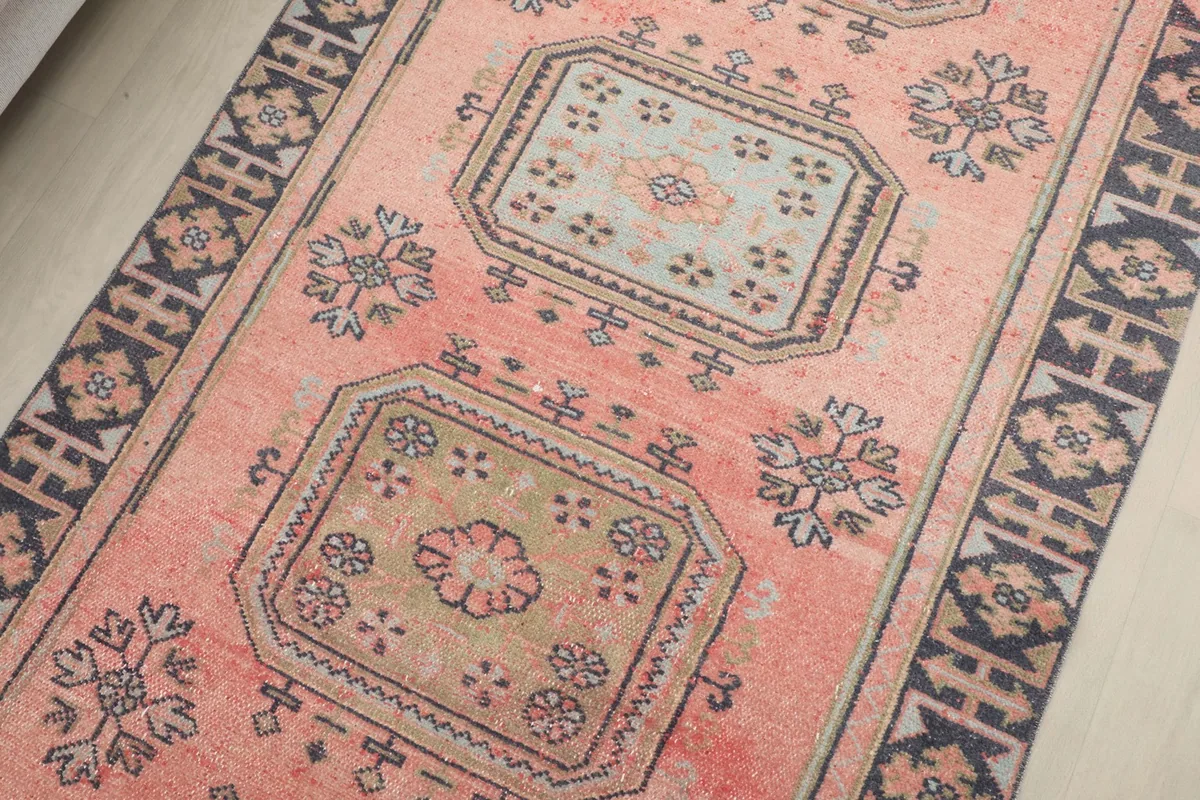 Detailed angle of the rug's center, showing various geometric motifs in rose, navy, beige, and olive